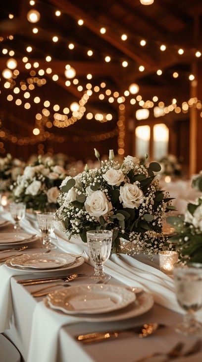 Stunning white wedding table with white roses and fairy lights Elegant Farmhouse Wedding Centerpieces, Reception Candles And Greenery, White Peonies Wedding Centerpieces, Fairy Light Wedding Table Decor, Wedding Round And Rectangular Tables, Wedding Table With Candles And Flowers, Green Cream And Gold Wedding Table Settings, Wedding Table Decorations White Roses, Candle Light Wedding Table