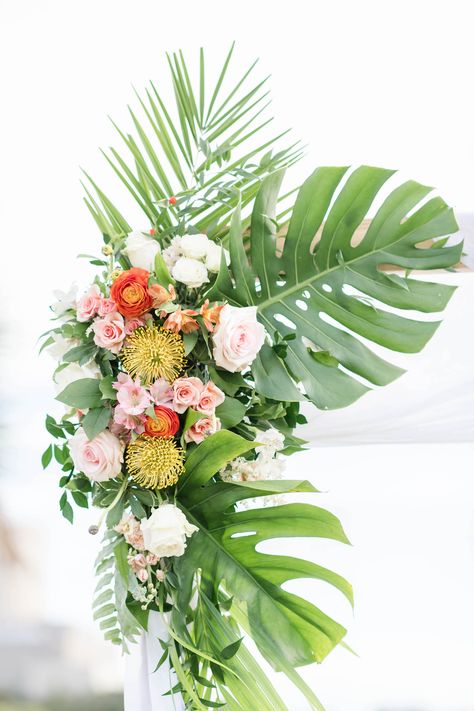 Tropical Wedding Ceremony Decor, Monstera and Palm Fronds, Pink and White Roses, Yellow Pincushion Proteas, Orange Floral Arrangement on Arch | Tampa Bay Wedding Planner Coastal Coordinating Orange And White Tropical Wedding, Palm Leaf Floral Arrangement, Monstera Floral Arrangements, Monstera Flower Arrangement, Tropical Floral Arrangements Wedding, Palm Floral Arrangements, Monstera Arrangement, Arbour Arrangement, Tropical Flower Arrangements Wedding