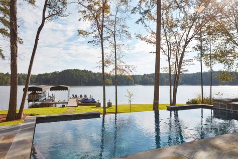 An enticing infinity pool offers peaceful views of Lake Oconee. The homeowners enjoy wakeboarding, water-skiing, and taking sunset cruises around the lake. Lakeside Pool Ideas, Infinity Pool Lake View, Pool By Lake, Waterfront Pool Designs, Pool Lake Backyard, Pool By The Lake, Lake House Backyard With Pool, Lake House With Pool, House Pool Ideas