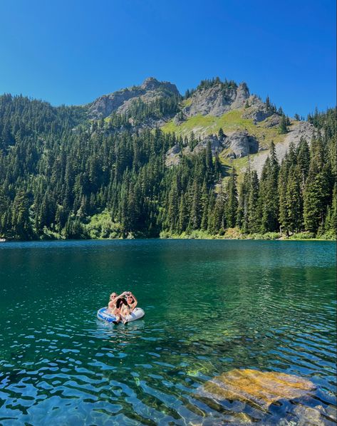 Two girls floating with an inner tube on an alpine lake. There are mountains in the background and it is a sunny day. Pacific Northwest Hikes, Mountains With Lake, Pacific Northwest Aesthetic, Sunny Mountains, Pacific Northwest Hiking, Pacific Northwest Summer, Sunnyvale California, Lake Swimming, Hiking Summer