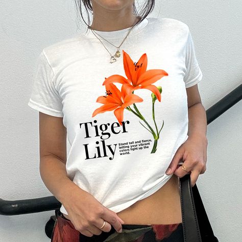 Unleash your wild side with our Vibrant Tiger Lily Graphic Baby Tee! This stunning shirt features a bold and beautifully detailed tiger lily graphic, perfect for adding a pop of color and a touch of nature-inspired elegance to your wardrobe. Crafted from soft, high-quality fabric, this tee offers a comfortable and flattering fit, making it an ideal choice for everyday wear or special occasions. Embrace the spirit of the tiger lily – fierce, vibrant, and unapologetically unique. Pair it with your favorite jeans or skirt for a standout look that captures the essence of Y2K style. Get ready to turn heads and express your inner flower power with this must-have piece! Key Features: Detailed tiger lily graphic design Soft, 100% Cotton Perfect for casual or dressed-up looks Embrace your bold, uni Lily Graphic, Baby Tee Aesthetic, Graphic Baby Tee, Baby Graphic Tees, 90s Baby, Trendy Top, Fitted Tee, Baby T Shirts, Tiger Lily