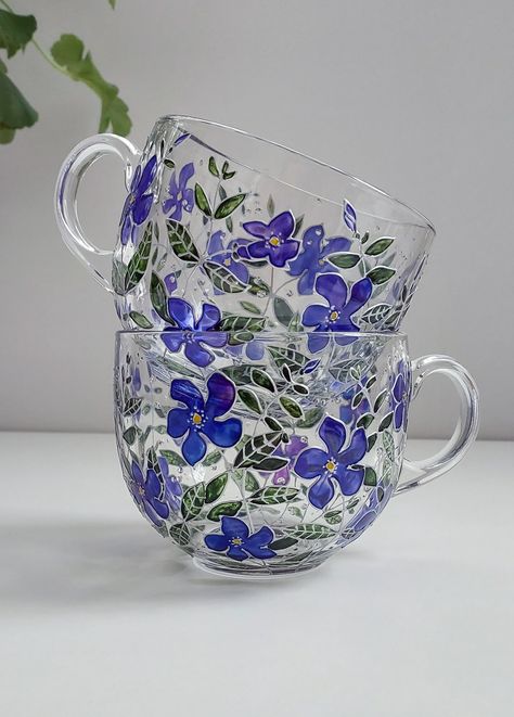 Microwave safe.This is a vibrant glass coffee mug set of 2 items with hand-painted cute periwinkle flowers. Everybody needs their very own cozy mug, obviously. If you need big cute mugs for a couple these nature-inspired botanical mugs are perfect for this. If you love hot drinks and nature, here is a mug that will make you happy. These beautiful rich colors glass coffee mugs are perfect for coffee or tea-obsessed persons who love nature. Treat yourself to something special. Christmas is a long way off, and you shouldn't have to wait that long for a present. Think of it as an investment in your productivity.  This cool cup set also happens to be one of the most popular gifting items - because it's both useful and thoughtful. This hand-painted glass mug set feature stems with flowers and le Hand Painted Glass Mugs, Hand Painted Glass Cups, Glass Cup Painting, Bottles Diy, Table Wear, Hand Painted Glassware, Glass Coffee Mug, Glass Painting Designs, Violet Flowers