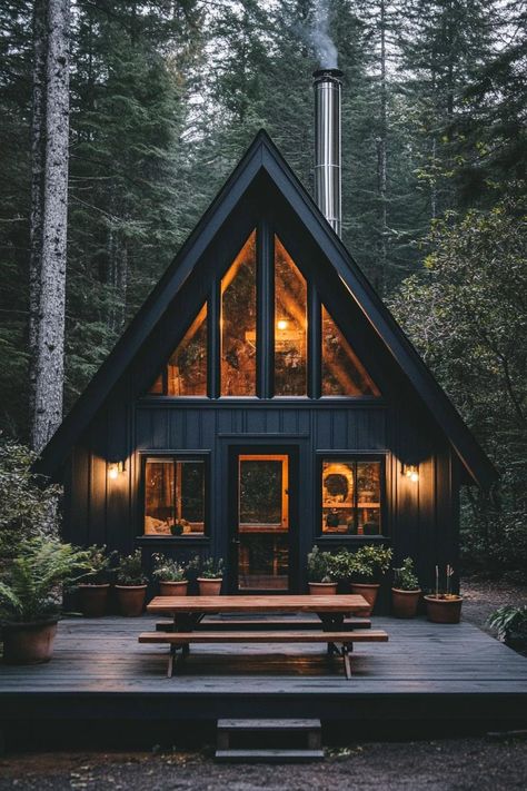 Front view of a modern a frame cabin in charcoal black siding full wall glass windows natural wood door with glass panels tall chromed chimney in. Check out all of these stunning and chic dark A-frame houses that pack a ton of charm into a small forest retreat. Log Cabin A Frame, Moody Modern Cabin, Small Black Cabin, A Frame House Ideas, Door With Glass Panels, Natural Wood Door, Wood Door With Glass, Dark Cabin, Black Siding