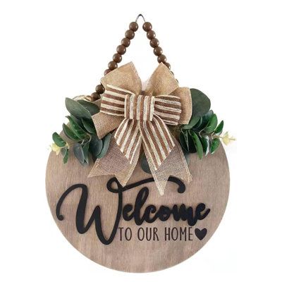 The "Welcome" design stands out with its unique 3D effect, complemented by a stylish buffalo check ribbon, lifelike green plants, and elegant silk flower accents. This charming combination adds a delightful touch to any entryway, making guests feel warmly invited! The Holiday Aisle® | The Holiday Aisle® 3D Wooden Hanging Welcome Sign - 12" Round for Home & Farmhouse Porch Decor in Oak Nature | 0.5" H X 12" W X 12" D | Wayfair Flower Logos, Hanging Welcome Sign, Farmhouse Porch Decor, Sign For Front Door, Porch Decorations, Welcome Design, Artificial Leaves, Signs Diy, Farmhouse Porch