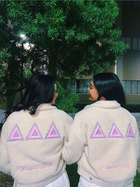 Two girls with their backs facing the camera. They are wearing white jackets with 3 pinks deltas while looking at eachother. Sorority Jackets Ideas, Sorority Jackets, Theta Merch, Aphi Merch, Paddle Ideas, Big Little Basket, Delta Delta Delta, Meeting Outfit, Delta Sorority