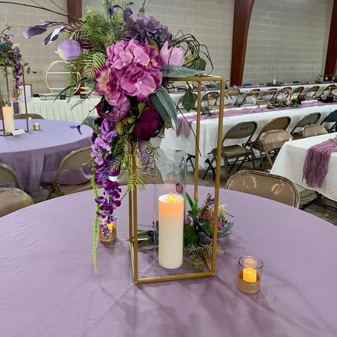 Brighten up your wedding tablescapes with chic table centerpieces and ooze magical flair all around. Dress up the tables in lavender tablecloth and create a visually appealing effect of height and dimension by setting gold flower stands decorated with a purple & lavender hued hydrangea, peonies, orchid stems, wisteria vines, & greenery spray flower arrangement. Highlight the majestic appeal of your tablescape by arranging LED pillar candles and votive candles in honeycomb base candle holders. Wisteria Table Decorations, Wisteria Centerpiece, Wisteria Vines, Event Decor Ideas, Party Decorations Table, Vines Flowers, Thanksgiving Breakfast, Orchid Centerpieces, Lantern Centerpieces