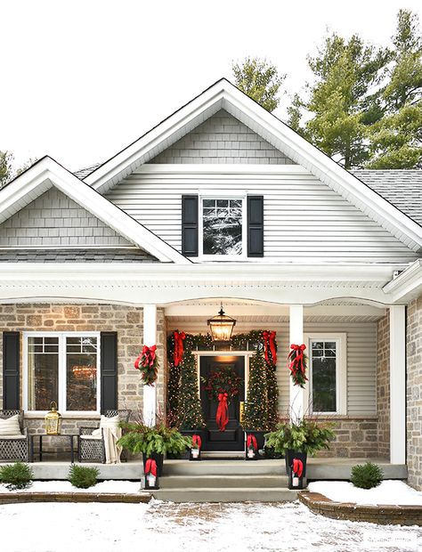 Christmas front porch decorated in classic greenery and red bows. Decorate Front Of House For Christmas, House With Columns Christmas Decor, Outdoor Christmas Decor Ranch Style House, Christmas Decorated House Exterior, Outdoor Traditional Christmas Decor, Large Outdoor Christmas Wreaths On House, Craftsman Christmas Porch, Long Porch Christmas Decor, Front Gate Christmas Decor