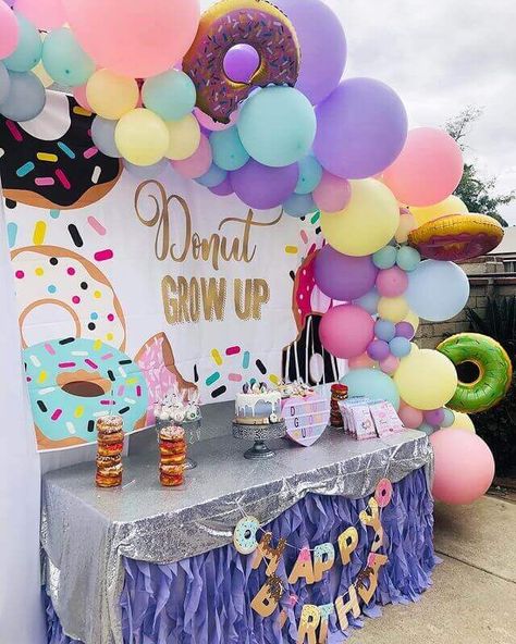 Glamorize your outdoor birthday party’s backdrop décor with a vibrant donut themed vinyl backdrop. Adorn the backdrop with yellow, pastel pink, turquoise, purple, pastel lavender latex balloons along with donut shaped Mylar balloons to form a balloon arch. Place the cake table in front of the backdrop and embellish it with a silver sequin tablecloth and a purple curly taffeta table skirt. Use a riser stand to host the birthday cake and place dessert display stands to serve other tasty treats. Donut Birthday Party Ideas, Outdoor Birthday Party, Donut Invitation, Event Decor Ideas, Donut Birthday Party, Dessert Display Stand, Donut Decorations, Outdoors Birthday Party, Donut Birthday Parties