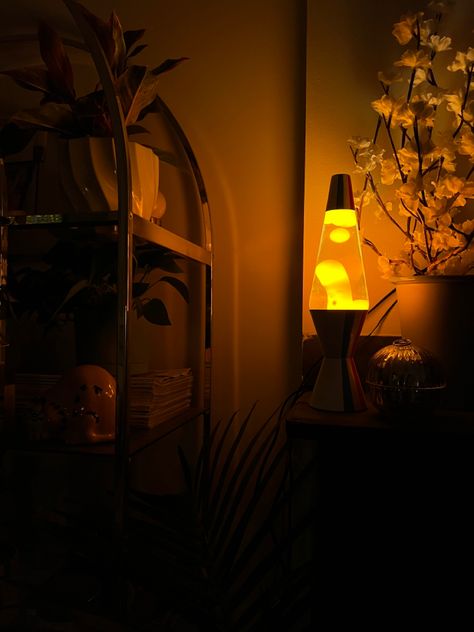 White lava lamp off-center to the right with orange lava flowing at night in the dark. Lamp is on a mantle to the left of a white floral display. There is a decorated golden arched shelf to the left of the mantle. Dark vignette creating a moody orange and black photograph. Bedroom Lava Lamp, Lava Lamp Decoration, Lava Lamp Living Room, Orange Candle Aesthetic, Warm Lighting Lamp, Mood Lamp Aesthetic, Lava Lamp Decor, Lava Lamp Aesthetic Room, Warm Lighting Aesthetic