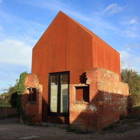 London architects Haworth Tompkins have inserted a Corten steel artist's studio into a ruined Victorian dovecote in Suffolk, UK. Called The Dovecote Studio, the structure has a pitched rood and occupies the same space as the original building's interior. A skylight in the north side of the roof illuminates the plywood interior, which includes a mezzanine with Prefab Metal Homes, Plywood Interior, Row Houses, Brick And Wood, Tiny Cottage, Small Buildings, Corten Steel, Brick Building, Prefab Homes