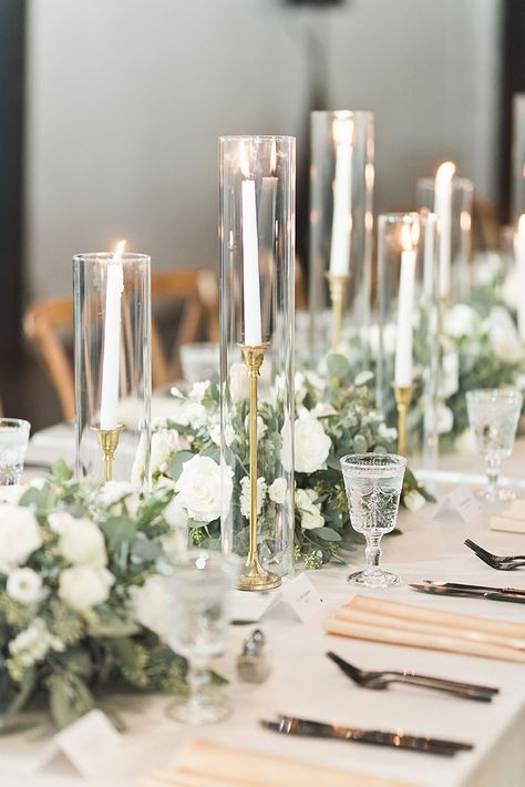 Candlestick In Glass Cylinder, Taper Candle In Glass Cylinder, Candle Sticks In Glass Cylinder, Tall Table Decorations Wedding, Enclosed Taper Candles Wedding, Tapper Candles Wedding, White Floral Centerpieces With Candles, Tall Candle Centerpieces Wedding, Wedding Esthetics