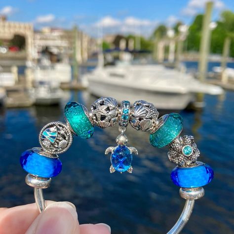 Happy Wednesday dear Pandora sisters!💙🩵💚😎 Today’s Ocean themed Pandora design at the Chelsea Harbor Marina features the lovely “Murano Glass Blue Sea Turtle” dangle charm as my centerpiece.🌊🛥️🐢 Included in my design are vintage classics from the Pandora Summer 2013 Collection, including a pair of the “Fascinating Aqua” muranos and the stunning silver “Sea Star”.💙🌊✨ I completed my styling with a pair of “Teal Shimmer” muranos, the “Ocean Life” charm and a pair of the silver Openworks with S... Pandora Ocean Charms, Blue Pandora Bracelet, Pandora Ocean, Pandora Summer, Pandora Design, Blue Sea Turtle, Pandora Bracelet Charms Ideas, Pandora Murano, Pandora Bracelet Designs