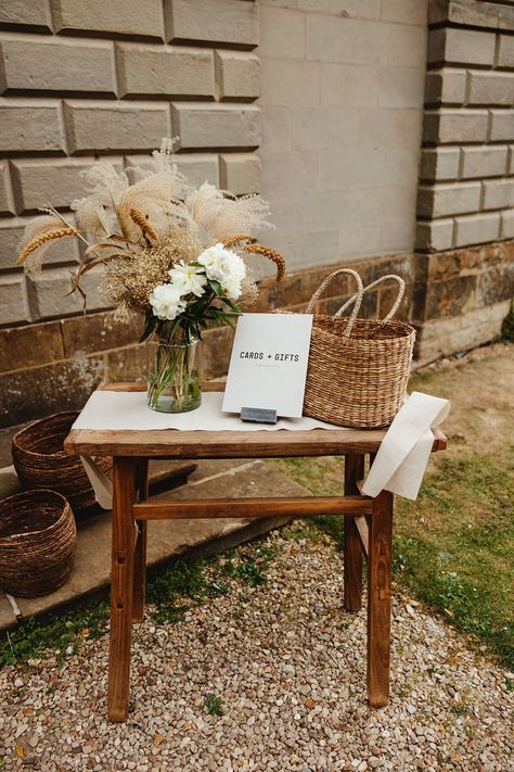 Wooden table and with flowers in glass vase and wicker basket with sign reading 'Cards Gifts' Picnic Basket Wedding Card Holder, Wicker Centerpiece Wedding, Gift Table Flowers Wedding, Boho Wedding Signing Table, Basket Card Box Wedding, Dried Flowers Wedding Decorations, Cards Gifts Table Wedding, Boho Guest Sign In Table, Cards Wedding Holder