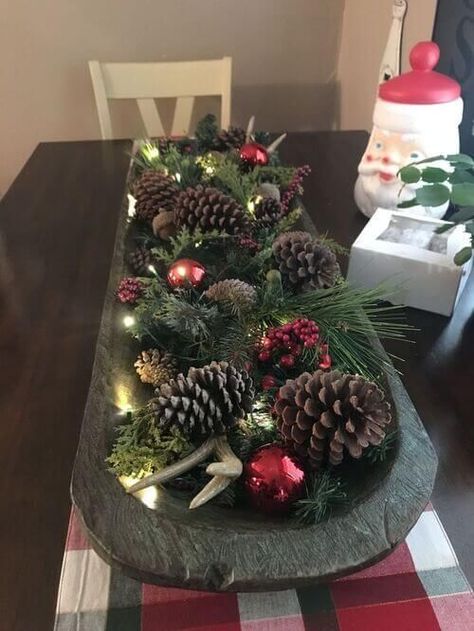 a Christmas arrangement of a dough bowl with evergreens, pinecones, ornaments, berries and lights Christmas Table Center Peice, Dining Room Table Centerpiece Ideas Christmas, Dough Bowl Centerpiece Christmas Decorating Ideas, Doughbowl Centerpiece Winter, Bread Bowl Decor Centerpieces Christmas, Bread Bowl Christmas Decor, Dough Bowls Decorated For Christmas, Wooden Bowl Christmas Decor, Christmas Dough Bowl Ideas