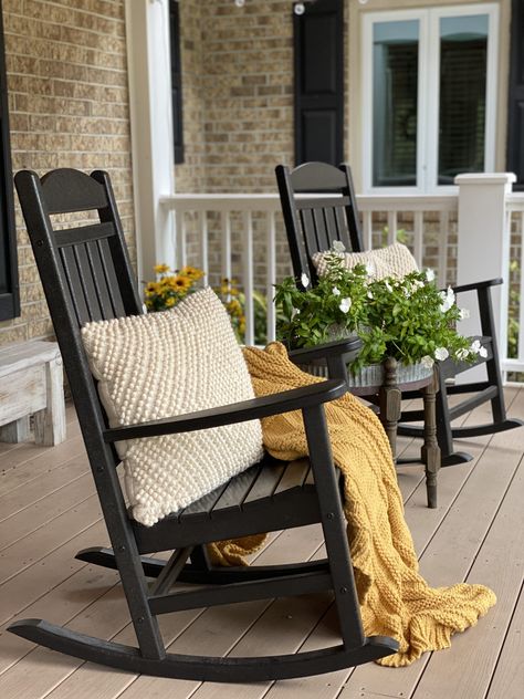 Front porch with black rocking chairs and a mustard yellow blanket, coat cream pillows and flowers. Porch With Black Rocking Chairs, Black Chairs Front Porch, Yellow House Front Porch, Black Porch Rocking Chairs, Black Outdoor Rocking Chairs, Rocking Chair On Porch Decor, Colorful Rocking Chair Front Porches, Rocking Chair Patio Ideas, Front Porch Black Rocking Chairs