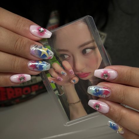 A picture of colorful nails with stars and chrome charms, holding a photocard of Le Sserafim's HUH YUNJIN with the same nails. Huh Yunjin Nails, Yunjin Lesserafim Nails, Le Sserafim Nails Inspired, Lesserafim Nails Inspired, Kpop Inspo Nails, Newjeans Inspired Nails, Le Sserafim Nails Designs, Le Sserafim Tattoo, Yunjin Nails