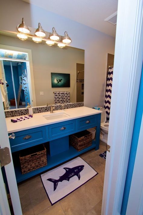 Fun shark themed bathroom with navy blue and white chevron shower curtain, shark picture, shark towels and floor mat.  A white quartz counter top with fun rock back splash.  The shower enclosure has rock starfish inlays and wavy gray stone walls. Jaws Bathroom, Surfer Bathroom, Shark Kids Room, Shark Rug, Shark Bathroom Decor, Bed With Bookshelf, Room Ideas Minecraft, Boy Room Ideas, Shark Shower Curtain