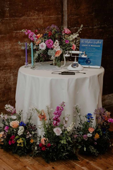 Round table with spring flower arrangements and rotary phone wedding guestbook with purple and teal tapered candles at Elmore Court Gloucestershire Audio Guest Book Table Decor, Audio Guest Book Table, Wedding Flowers Round Table, Audio Guest Book Wedding, Flower Decorations Wedding, Colourful Wedding Flowers, Guest Book Table Decor, Groom And Groomsmen Outfits, Wedding Welcome Table