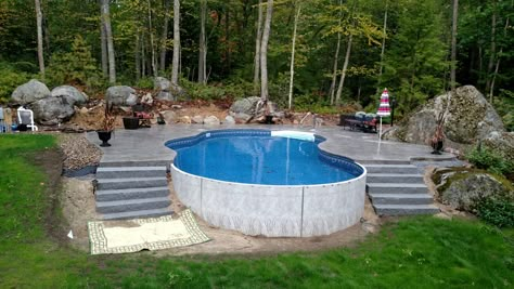 Radiant 18x32 Freeform built into a hill with stamped concrete deck and walk-in steps Pool In Side Of Hill, Above Ground Pools Built Into Hillside, Above Ground Pool Deck Ideas Sloped Yard, Above Ground Pool On Hill, Pool In Sloped Backyard, Above Ground Pool Built Into Hill, Pool In Hillside, Pool Built Into Hill, Pools Built Into Hillside