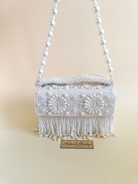 Make a statement of timeless elegance with this stunning handmade white pearl beaded purse, designed with intricate floral patterns and delicate fringe details. Perfect as a bridal bag for weddings, an evening accessory, or a thoughtful gift for her, this purse combines functionality with unmatched artistry. The bag is carefully crafted using high-quality pearl beads, making it a luxurious choice for brides, partygoers, or anyone seeking a standout piece for special occasions. The purse features a secure magnetic closure and a single compartment lined with soft fabric to keep your essentials safe. Its pearl-beaded strap allows it to be carried as a shoulder bag or clutch, adding versatility to its sophisticated design. Whether you're looking for an evening clutch to complete your formal lo