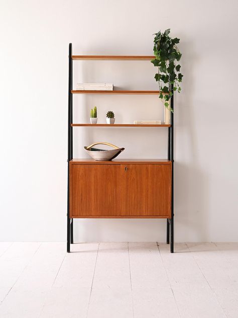 Enhance your living space with this authentic Scandinavian bookshelf from the 1960s, a stunning example of Swedish mid-century design. Dimensions: Width: 75cm (29.52inch) Height: 157 cm (61.81 inch) Depth: 40cm (15.74inch) Crafted from warm teak wood, this bookshelf features a sleek black-painted frame, offering a striking contrast that adds sophistication to any room. The unit is designed with three spacious shelves, perfect for displaying books, art, or decorative items, along with a lower cabinet equipped with hinged doors, providing concealed storage for additional items. The minimalist and functional design, characteristic of Nordic style, ensures this bookshelf seamlessly blends into modern and vintage-inspired interiors. In good condition with some signs of age, this piece has been Scandinavian Bookshelf, Displaying Books, Wood Shelving Units, Wood Shelving, Concealed Storage, Inspired Interiors, Vintage Scandinavian, Low Cabinet, Books Art