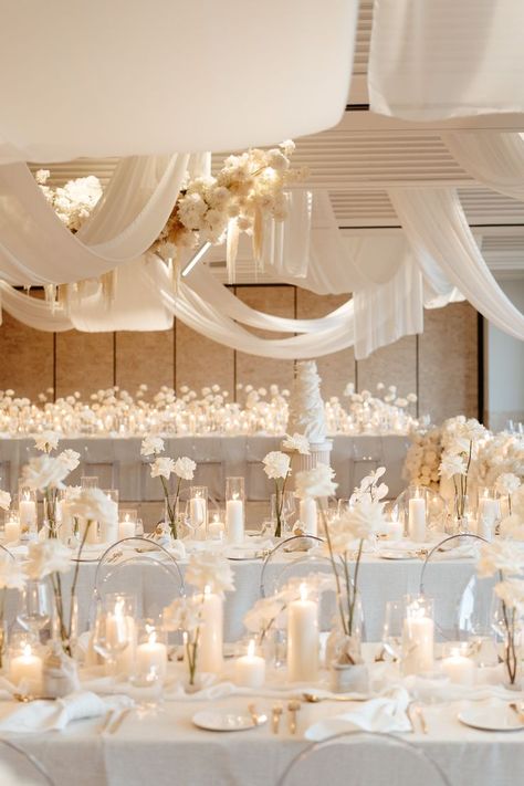 All white wedding. White Pillar Candles, white garden roses and orchids, and gold silverware. White Cream Ivory Wedding, Off White Wedding Decorations, Minimal Center Piece Wedding, White And Glass Wedding Decor, White Neutral Wedding Decor, White And Candle Wedding, Ivory Decor Wedding, Ivory Party Decorations, Rose Gold White Wedding Decor