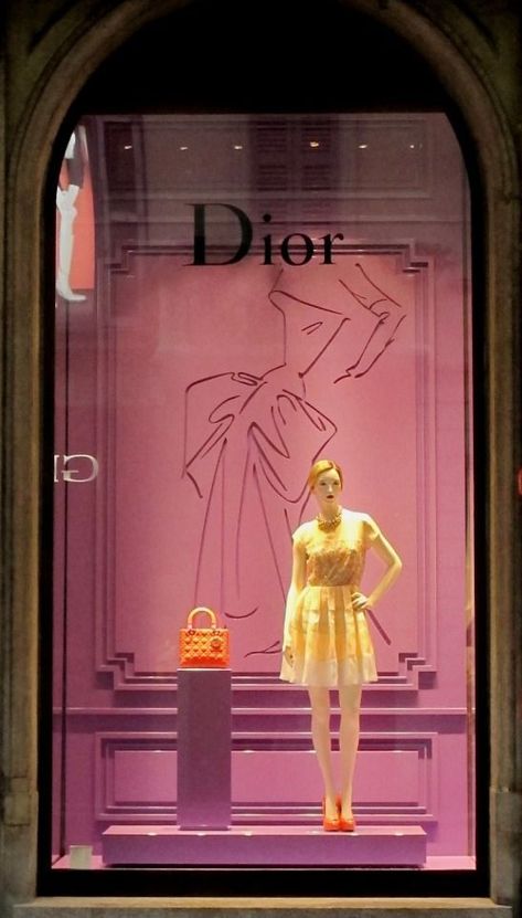 When I speak of the term color, the designer use bold colors such as yellow, orange and light purple. The dress and the purse stands out. For scale, it is comparing the size of the purse to the mannequin standing next to it. The purse is very small, whereas the mannequin is tall. Line and composition is represented in the background with the drawing of the dress behind the mannequin and purse. It looks like the shape of a dress women would wear in the old days Day In Milan, Fashion Window Display, Luxury Windows, Store Design Boutique, Visual Merchandising Displays, Window Display Design, Retail Windows, Store Windows, Store Window