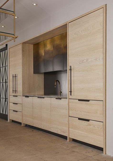 This fully functional Ombré Kitchen pairs modern appliances with Amuneal’s artisanal hand finishes. Bleached oak with oxidized bronze hardware surround a concealed refrigerator, dishwasher and full pantry with retractable doors. The hand-patinated ombré upper cabinetry transitions from bright to dark brass, with integral dimmable LED under cabinet lighting. #kitchenideas #homedecorideas #kitchen Waterfall Island Kitchen, Wall Mounted Shelving Unit, System Furniture, Led Under Cabinet Lighting, Modern Appliances, Kitchen Installation, Oak Kitchen, Custom Kitchens, Bronze Hardware