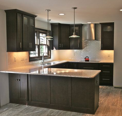 Modern kitchen with shaker cabinetry in a dark wood finish. Accented by light granite countertops, sleek pendant lights and a white subway tile backsplash in a herringbone pattern. Ebony Kitchen Cabinets, Herringbone Backsplash Kitchen, Kitchen Remodel Dark Cabinets, Backsplash With Dark Cabinets, Trendy Kitchen Backsplash, Granite Countertops Kitchen, Dark Kitchen Cabinets, Dark Cabinets, Gorgeous Kitchens