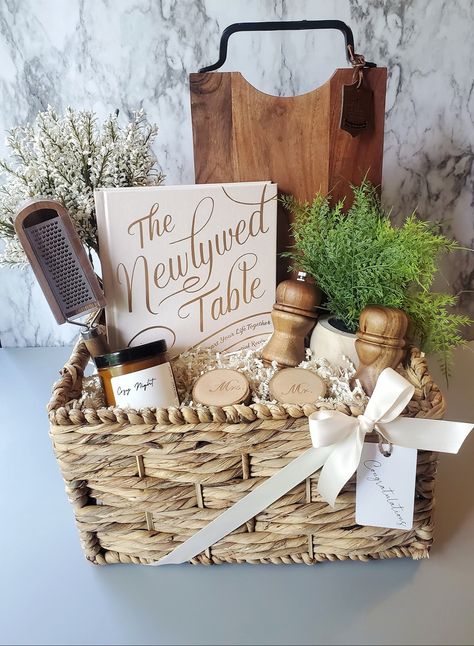 A charming custom wedding gift basket for a beautiful new couple celebrating their special day! Filled with some rustic items for their new home and a cookbook to inspire couples to cook as a team! #weddinggiftideas #weddinggiftideas #weddinggiftbasket #weddinggiftbasketideas #giftsforcouples Move In Gift Basket Ideas, Newly Wed Gifts Ideas Couple, Gift Basket For Bride And Groom, Game Night Wedding Gift Basket, Gift Basket With Purse, Newlywed Basket Ideas, Engagement Party Basket Gift, Wedding Shower Basket Ideas, Bridal Shower Box Gift