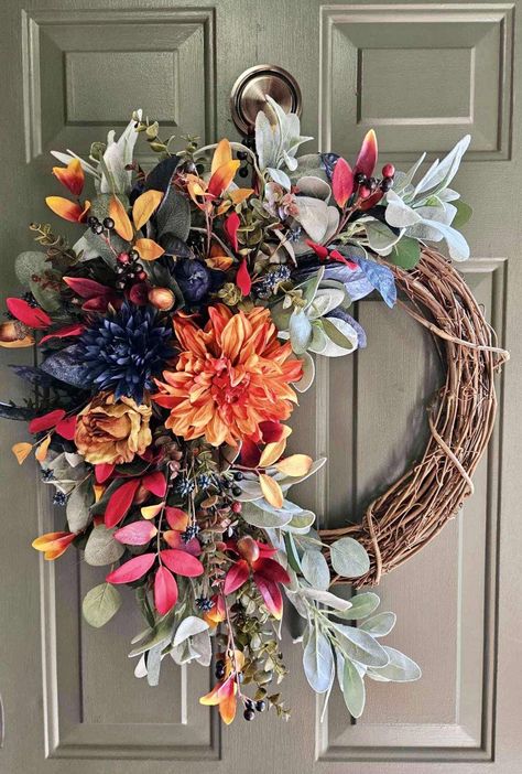 This fall wreath features a striking combination of vibrant orange and deep navy flowers, creating a bold and elegant contrast. The orange flowers, reminiscent of autumn leaves, add warmth and richness, while the navy blooms introduce a modern and sophisticated touch. Nestled among the flowers are delicate accents of red and gold foliage, warm toned acorns, and faux berries, enhancing the seasonal theme. The wreath is crafted on a sturdy grapevine base, with a natural, slightly asymmetrical design. Perfect for hanging on a door, enhancing a feature wall, or suspending over a fireplace, capturing the essence of fall in a chic, contemporary style. This wreath is made of high quality faux florals, and was designed on an 18 inch grapevine. Finished design measures approximately 23" W x 27" H x Modern Fall Wreaths For Front Door, Wreath Above Fireplace, Orange Fall Decor, Autumn Diy, Gold Foliage, Grapevine Wreaths, Door Wreaths Diy, Swag Wreath, Navy Flowers