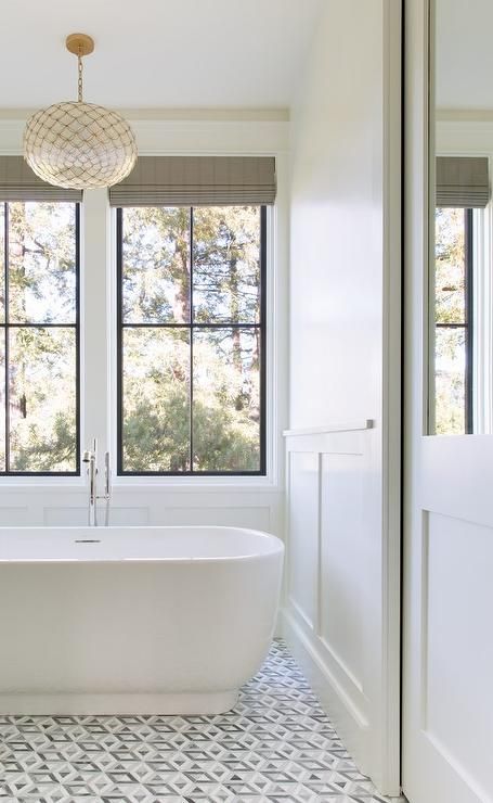 Serena & Lily Capiz Scalloped Chandelier above an oval tub in a master bathroom fitted with geometric white and gray floor tiles. Bathroom Wainscoting, Wainscoting Bathroom, Gray And White Bathroom, Window Seat Storage, White Bathroom Decor, Bathroom Remodel With Tub, Classic Bathroom, Trendy Bathroom, Traditional Modern