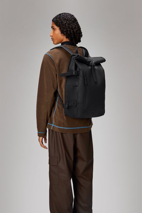 Rolltop Rucksack Large is a dependable city staple. The design interprets Rains' most iconic Rolltop Rucksack with larger proportions and additional functionality. Rolltop Rucksack Large is carefully designed to keep precipitation out when traveling from point A to Z. To protect essentials from rain, fold the rolltop into a tight scroll and secure using the signature carabiner. Open the rucksack to reveal a single main compartment. Exterior features include a side-access laptop pocket, front poc Rains Bag, Rains Backpack, Divine Union, Popular Backpacks, Picnic Accessories, Holiday Wishlist, Leather Backpack For Men, Commuter Backpack, Backpack Outfit