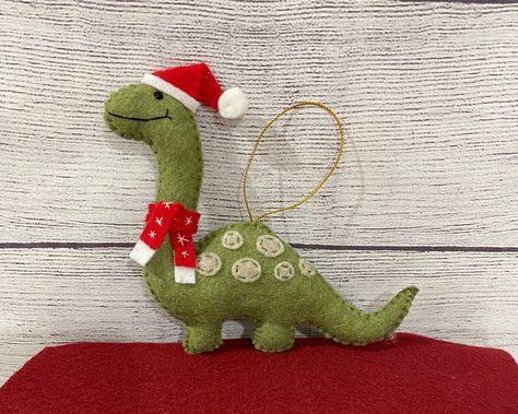 "These dinosaurs are all ready for Christmas with their little Santa hats and festive scarves, all hand sewn!! What a fun gift or stocking stuffer for that dinosaur lover in your life!! Kids will love putting this special festive dinosaur on their Christmas tree each year. Each Santa-sarus ornament is hand sewn, made from felt and stuffed with nonallergenic fiberfill. Our dinosaurs measure approximately 5\" tall and are one sided (no spots or face on back of ornament). Please feel free to ask for different colors.  We're happy to accommodate color changes. Hangers vary (gold or silver). Shipping:  When possible we recycle and reuse shipping boxes. Reusing boxes reduces your shipping costs and helps the environment! Our dinosaurs are made in a smoke-free and pet-free home. Facebook: www.fac Dinosaur Felt Ornaments, Crochet Christmas Dinosaur, Felt Dinosaur Ornament, Diy Sewn Christmas Ornaments, Felt Dinosaur Pattern Free, Felt Christmas Ornaments Patterns Free, Felt Christmas Ornaments Diy, Easy Felt Christmas Ornaments, Felt Christmas Ornament Patterns