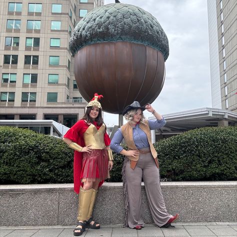 First Image: Two cosplayers, portraying the tiny cowboy and roman soldier from the Night at the Museum films, stand in front of a giant Acorn appearing smaller by proxy!
Second Image: A medal won by the two cosplayers being held in their hands. On the gold medal is a rocket taking off and the convention name "Galaxycon", behind the hands are blue and red costume fabrics as well as the Romans Helmet and the Cowboys Fake Gun. The hands are adorned with a red bandanna(left) and gold armor(right) Jedediah And Octavius, Night At The Museum, Comic Con Cosplay, Best In Show, Roman Soldiers, Couple Halloween, Couple Halloween Costumes, Grad Parties, Couples Costumes