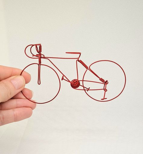 Good morning ! Here is an entirely handmade miniature bicycle, made from wire then painted with red spray paint then a little varnish. It measures approximately 12 cm in length, 6.5 cm in height and is ideal for window or wall decoration for bike enthusiasts :) Made with passion, it is made up of 3 wires, one long for the whole thing and the other 2 for the pedals and the stand. The wheels don't turn but the pedals do. There is no gluing, it is assembled using a wire bending system using pliers. Welded Bicycle Art, Wire Art Bike, Sculpture Wire Art, Sculpture Wire, Wire Bending, Red Spray Paint, Cyclist Gifts, Bicycle Painting, 3d Pen