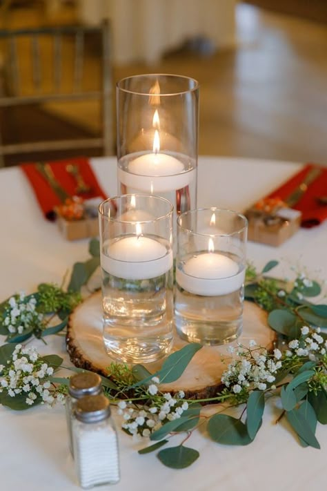 rustic fall wedding reception centerpiece with a wood slab surrounded by greenery and topped with vases with floating candles Floating Candles On Wood Centerpieces, Round Wood Centerpiece Wedding, Wood Slab Centerpieces, Floating Candles Wedding Centerpieces, Burnt Orange Fall Wedding, Floating Candles Mason Jars, Candle Votive Centerpiece, Wood Centerpieces Wedding, Orange Fall Wedding