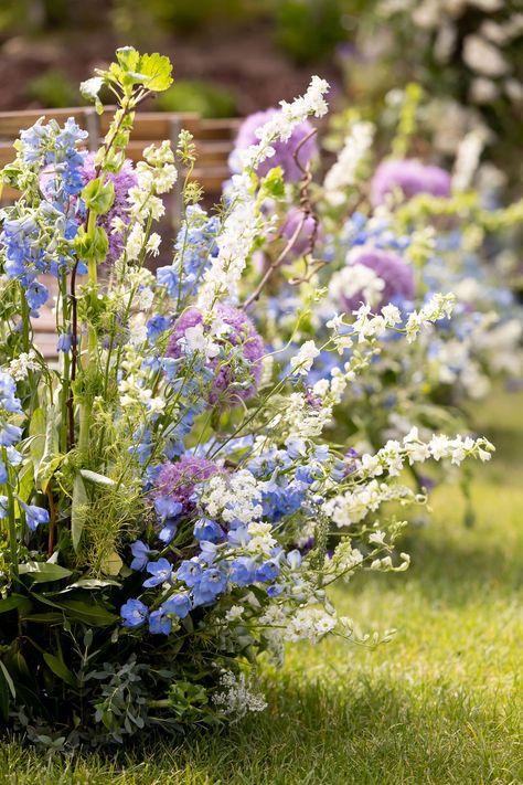 Blue delphinium, white larkspur, giant purple allium, bells of ireland, kiwi vine, lysimachia, queen anne's lace ceremony aisle floral hedge White Green Purple Blue Wedding, Delphinium Wedding Aisle, Allium Wedding Flowers, Blue Purple Yellow Wedding, Blue Purple Green Wedding Color Palettes, Blue Delphinium Wedding, Wedding Ceremony Aisle Flowers, White Wildflower Wedding, Wildflower Wedding Ceremony