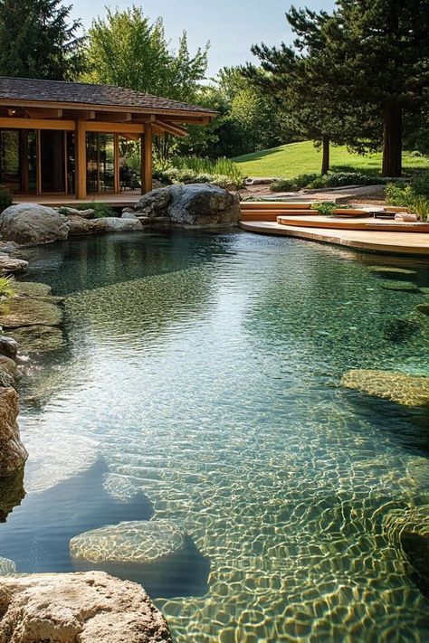 Create a natural swimming pool that blends with your landscape. Discover the benefits of eco-friendly pools that use plants and natural filtration systems. 🏊‍♂️🌱 #NaturalSwimmingPool #EcoFriendlyLiving #SustainableDesign Zen Swimming Pools, Lagoon Style Pool Backyards, Pond Like Swimming Pools, Natural Pool Aesthetic, Lagoon Style Pool Ideas, Natural Lake Pool, Log Cabin Pool Ideas, Natural Pool Backyard, Natural Inground Pool