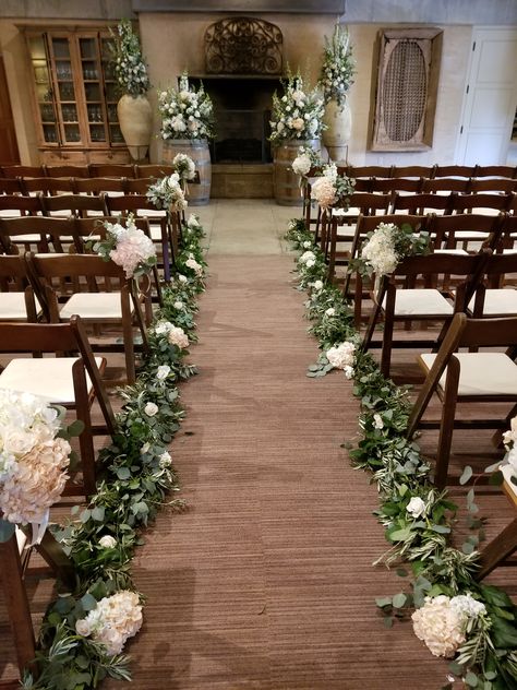 Sonoma Wedding Ramekins - Indoor wedding aisle floral featuring eucalyptus garland lining the aisle dotted with ivory and blush flowers. Chair bouquets, Altar flowers on wine barrels. #Ramekinswedding #Sonomawedding #aislefloral #winebarreltoppers Wedding Aisle Garland Decor, Eucalyptus Aisle Runner, Eucalyptus Lined Aisle, Wedding Aisle Garland, Wedding Aisle Eucalyptus, Wedding Aisle Indoor Decorations, Wedding Aisle Florals Indoor, Elegant Aisle Decorations Wedding, Chair Aisle Decor Wedding