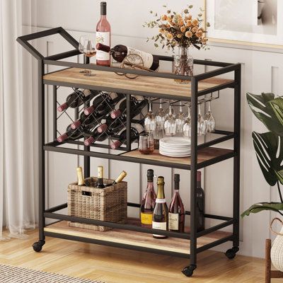 From the living room to the dining room, this bar cart is an ideal addition to your home. It is equipped with a wine rack and stemware rack. And 3 large shelves provide plenty of space to hold liquors, snacks, glassware, silverware, or cleaning supplies. Each shelf has wraps-around bars to keep your items safe. This bar serving cart can easily roll from room to room on the 4 castors, 2 of which lock into place. The clean-lined design will add an updated feel to your space, while a neutral finish helps it blend with a variety of colour palettes and aesthetics. | 17 Stories Tyanna Industrial Bar Cart black/Brown 36.22 x 35.62 x 14.17 in, Manufactured Wood | C009516784_1766722587_1791823513 | Wayfair Canada Industrial Bar Cart, Wine Cart, Bar Serving Cart, Metal Bar Cart, Liquor Bar, Stemware Rack, Apt Ideas, Serving Cart, Industrial Bar