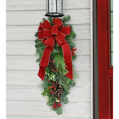 This beautiful pine door swag can be used on a door, an outside light fixture, mantel decoration, stair railings or windows to enhance your holiday season. Get more than one! Created with artificial pine, pine cones, berries and a handmade red velvet bow with gold edge. The Holiday Aisle® | The Holiday Aisle® Faux Pine Teardrop Swag 36.0 H x 5.0 W x 10.0 D in green / red | 30" H X 9" D X 10" L | Wayfair Christmas Swag Outdoor Light, Red And Green Outdoor Christmas Decor, Christmas Swag For Outdoor Lights, Swag Door Wreath, Indoor Christmas Door Decorations, Christmas Teardrop Wreath, Christmas Window Swags Outdoor, Diy Swag Wreath, Christmas Swags For Front Door