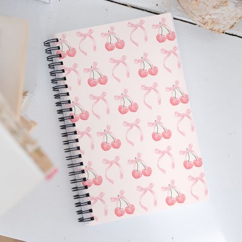 Coquette Aesthetic Notebook with pink cherries and ribbons. Product information: * Covers with soft-touch coating * Cover weight: 10.38 oz/yd² (352 g/m²) * Page weight: 2.62 oz/yd² (89 g/m²) * Metal wire-o binding * 140 dotted pages * US fulfilled notebooks measure 5.5″ × 8.5″ (13 × 21 cm) * EU fulfilled notebooks measure 5.7″ × 8.5″ (14.5 × 21 cm) * Blank product sourced from the US and Sweden This product is made especially for you as soon as you place an order, which is why it takes us a bit Cute Back To School Supplies, Girly Journal, Coquette Cherry, Daughter Style, Gifts For Students, Notebook Cute, Pink Notebook, Cherry Pattern, Dotted Page