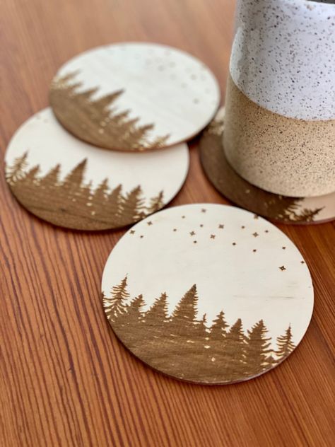 "Every coaster in a set comes with a beautiful pine tree and starry sky scene engraved on one side. The wood coasters compliment any living space quite well, regardless of style. The unfinished surface of the wood slices makes the perfect coaster, keeping furniture safe from moisture and heat given off by mugs or glasses. Coaster Details: - 1/8\" thick high-quality Baltic Birch - 4\" in diameter - Laser engraved pine trees and star silhouettes The burnt wood surface is laser engraved, giving eac Homemade Coasters Wood, Engraved Wood Coasters, Homemade Coasters, Nice Tattoos, Bird Coasters, Star Silhouette, Burnt Wood, Laser Engraved Ideas, Gray Jewelry