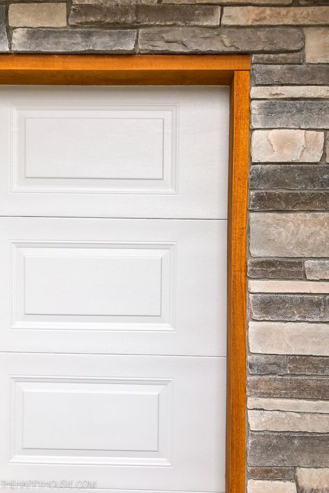 A white garage door, cedar trim and stone work. Wood Trim Around Garage Door, Wood Trim Garage Door, Cedar Trim Around Garage Door, White Garage Doors With Black Trim, Cedar Door Trim, Garage Trim Ideas Exterior, White House Cedar Accents, Cedar Trim Exterior, Garage Door Trim Ideas