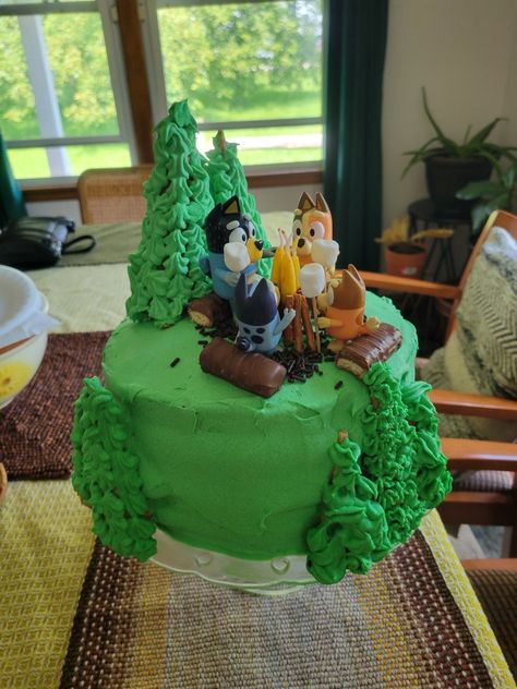 Bluey camping birthday cake with green frosting, waffle cone trees and a campfire of pretzels and birthday candles. Bluey Camping Cake, Bluey Camping, Cabin Cake, Camping Birthday Cake, Campfire Birthday, Camping Cake, Camp Birthday, Camping Cakes, Birthday Camping