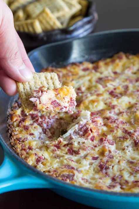 A photo of a wheat cracker being held up to the camera with hot Reuben Dip in the cracker. The dip is in the background and it is against a dark counter top. Hot Dip Recipes, Hot Reuben Dip, Reuben Dip Recipe, Reuben Dip, Classic Sandwich, Corned Beef Recipes, Reuben Sandwich, Snack Dip, Buffalo Chicken Dip