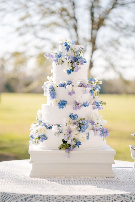 Multi-tier wedding cake decorated with blue, white and purple flowers. Photo: @alishacrossleyphotography Lavender And Blue Wedding Cake, Pastel Blue And Lavender Wedding, White Blue And Purple Wedding, Wedding Themes Blue And Purple, Purple And Blue Wedding Cake Ideas, Wedding Cakes Blue And Purple, Pastel Blue And Purple Wedding Theme, Light Blue Lavender Wedding, Pale Blue And Purple Wedding