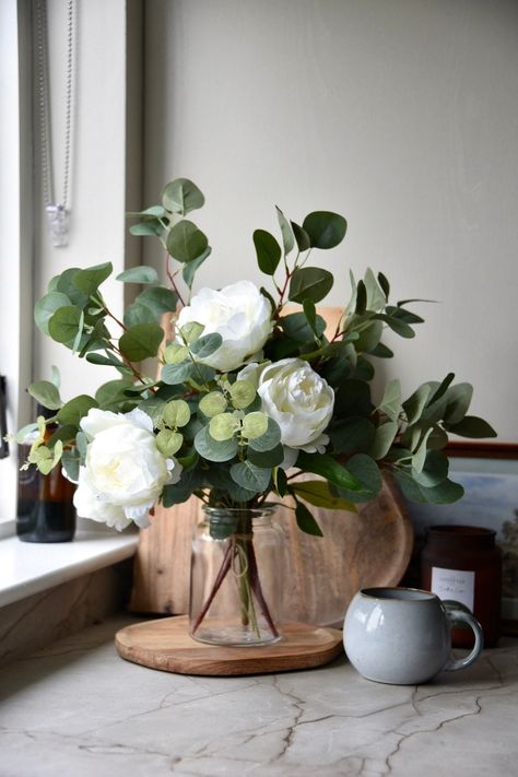 This beautiful ivory floral arrangement is very realistic.  It includes large peony roses and eucalyptus It is internally wired so that it can be bent to retain the desired shape.  Beautiful paired with a simple vase. This faux flower arrangement is timeless and made to fit into any home, whether it be a farmhouse, modern decor or simplistic.  An alternative use is wedding centre pieces or decor as they are elegant and timeless. All flower arrangements are handmade in Northern Ireland.  Options: Flower Arrangement With Eucalyptus, Peony And Eucalyptus Centerpiece, Simple Faux Flower Arrangements, Peony Floral Arrangements Wedding, Fall Themed Floral Arrangements, Sage Green Flower Arrangements, Large Faux Flower Arrangements, Flower House Decor, Kitchen Flowers Decor