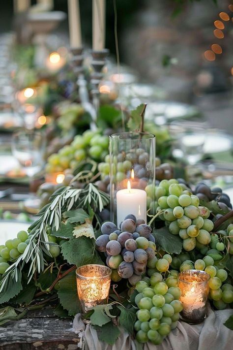 ✨ Elevate your wedding ambiance with a centerpiece that whisks you away to the rolling hills of Tuscany. Experience the charm of Italy as grape vines & olive branches intertwine with the warm glow of candles on your special day. #WeddingInspiration #TuscanWedding #RomanticDecor #WeddingIdeas #CountryChic #RusticElegance #GrapeAndOlive #CandlelightMagic Let the light guide your love story. Grapevine Wedding Decor, Grape Vines Decor Ideas, Olive Leaf Centerpiece Wedding, Wedding Table Olive Branch, Grape Centerpiece Wedding, Grapes On Wedding Table, Vineyard Table Decor, Olive Theme Wedding Table Settings, Tuscan Wedding Centerpieces